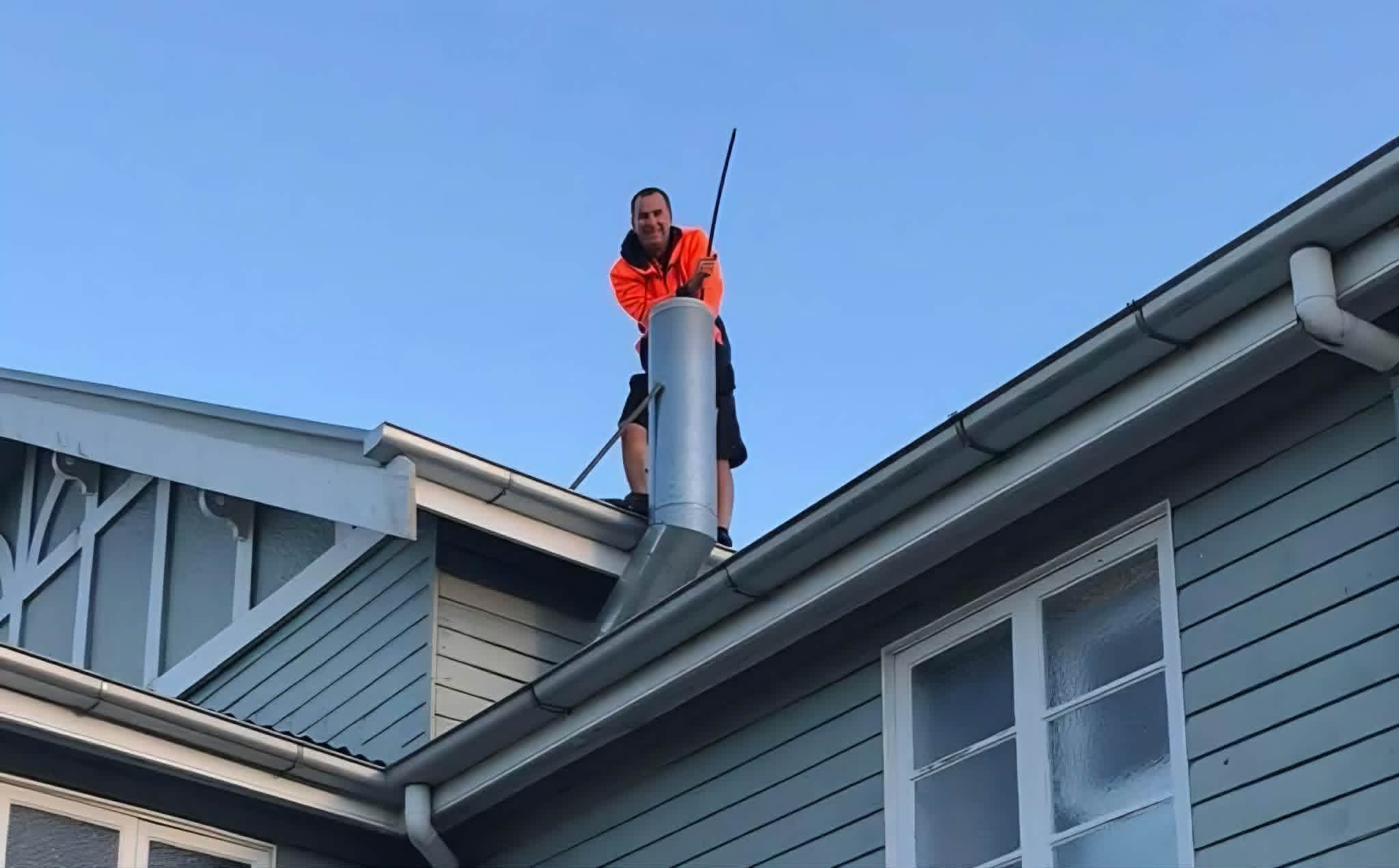 Gold Coast Fireplace Services technician on a roof, sweeping a flue with rods